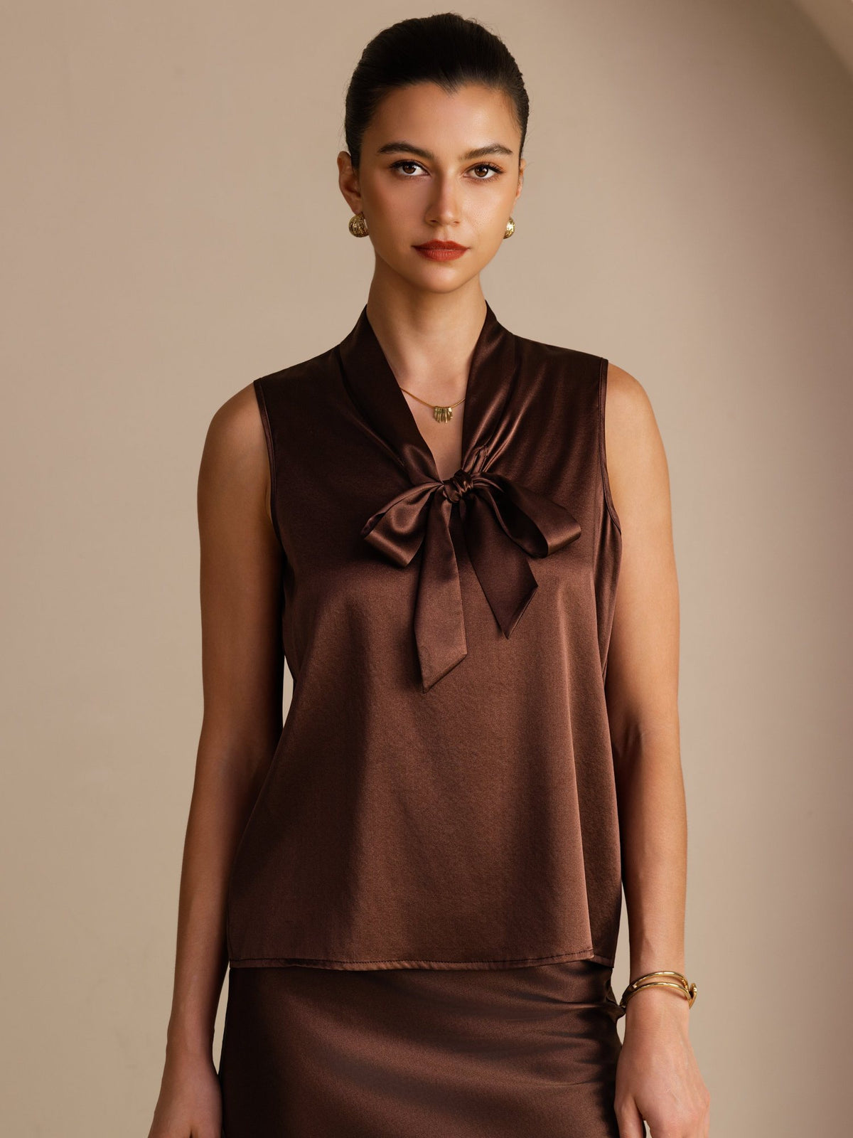 [Bitter Chocolate] Dark brown sleeveless tie-neck top on a model in a mid-length front view with arms relaxed and shoulders square. 001
