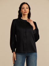 [Black] Black round-neck lantern-sleeve blouse on a model in a mid-length front view with one hand lifted near the neckline. 004