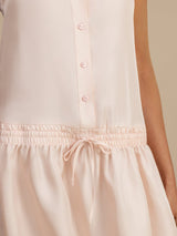 [Pink] Close waist view of a blush-pink drop-waist dress, showing the button placket, drawstring tie, and gathered skirt. 005