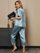 [Steel Blue] steel blue short-sleeve notch-collar pajamas with ankle pants and piping, full front view, dark book held at torso. 005