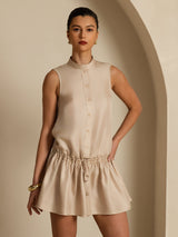 [Tan] Front three-quarter crop: tan sleeveless drop-waist mini dress with gathered ruffle hem, with one arm bent. 001