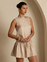 [Tan] Straight waist-up view: tan sleeveless drop-waist mini dress with gathered ruffle hem, with both arms down. 004