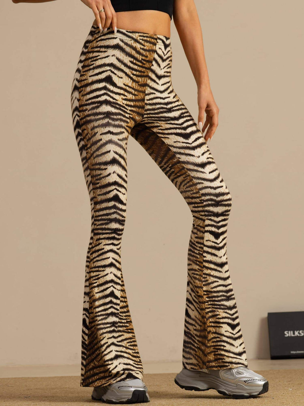 [Tiger] Mid-length front crop: high-rise flared trousers with a brown-and-black tiger stripe print, with one arm lifted. 001