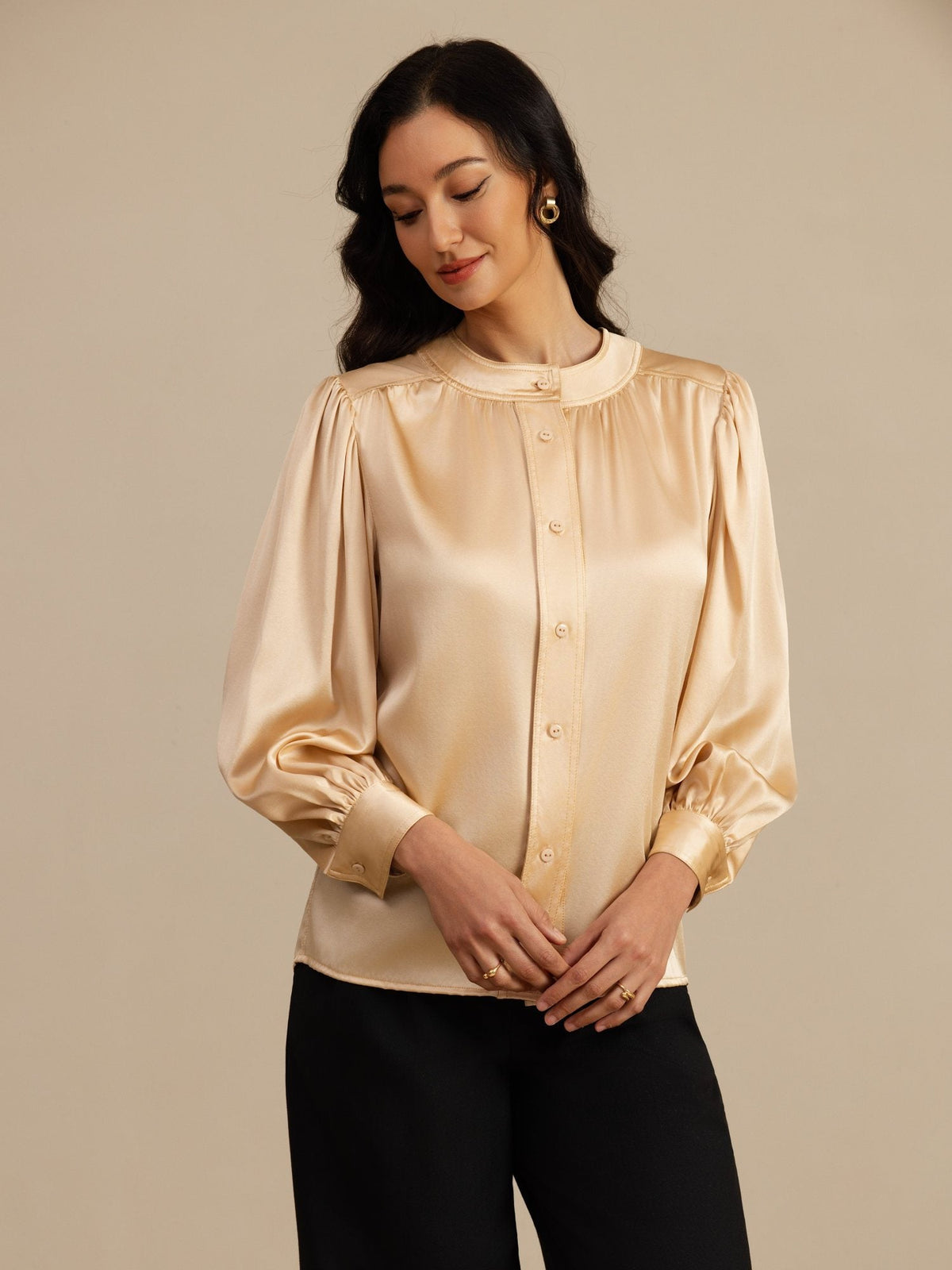 [Champagne] Champagne round-neck lantern-sleeve blouse on a model in a mid-length front view as she looks down toward the garment. 001