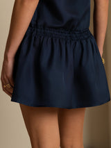 [Dark Blue] Close studio view of a model wearing a navy sleeveless drop-waist mini dress with a gathered ruffle hem. 005