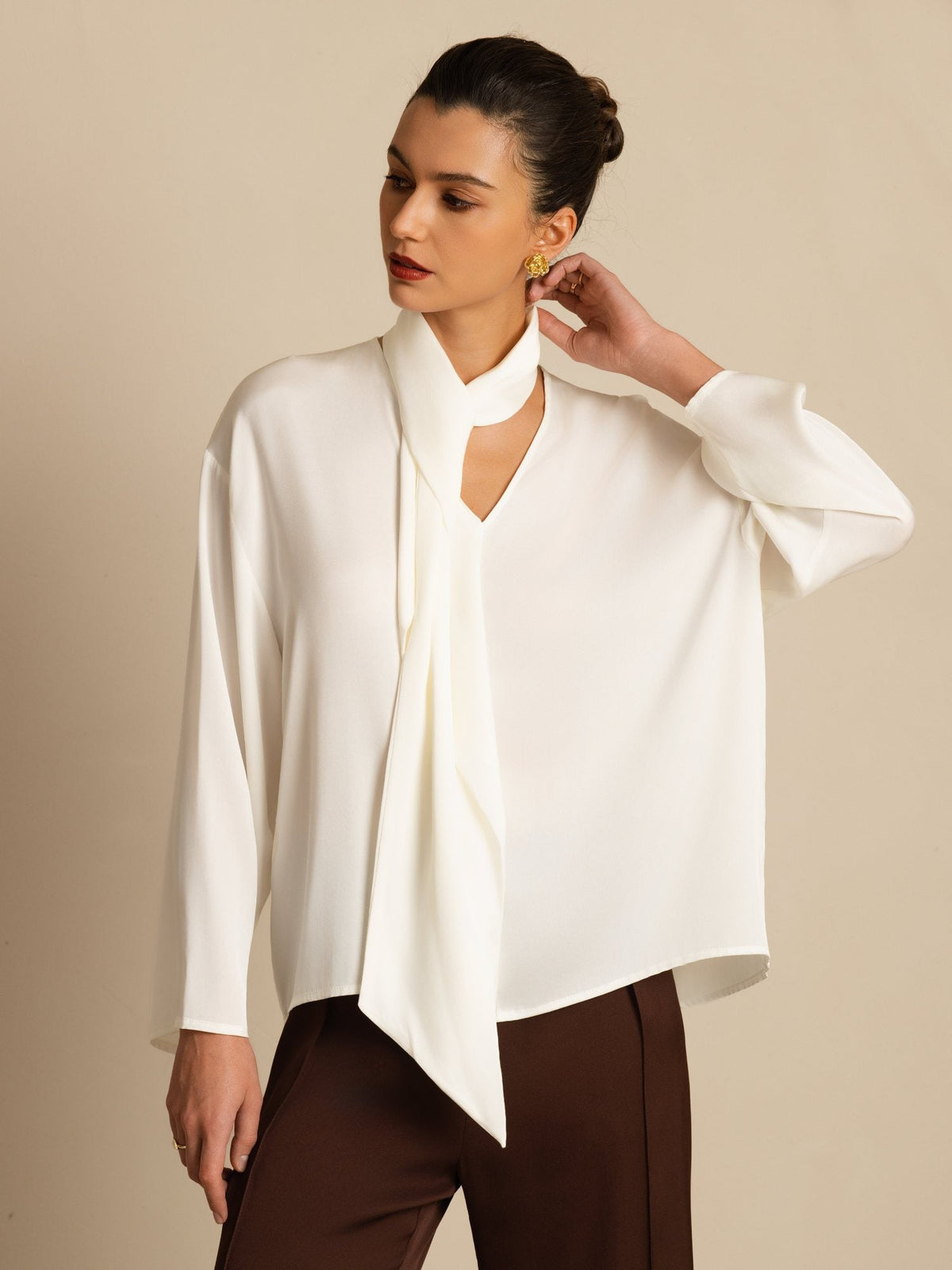 [White] Frontal mid-length frame: white draped-neck long-sleeve blouse with dark brown wide-leg trousers, with one arm bent. 001