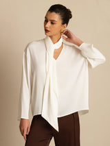 [White] Frontal mid-length frame: white draped-neck long-sleeve blouse with dark brown wide-leg trousers, with one arm bent. 001