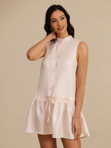[Pink] Angled view: blush-pink sleeveless drop-waist mini dress with gathered ruffle hem, with the model turned sideways. 003