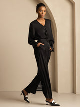 [Black] Full front view of black wide-leg trousers and a black blouse, both hands in pockets and one leg extended. 008