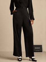 [Black] Black wide-leg trousers with a black blouse appears in a front mid-length crop, with one arm bent beside the torso. 001