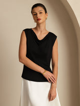 [Black] Black cowl-neck top with a white maxi skirt in a front crop to thighs, one arm reaching across to the opposite wrist. 004