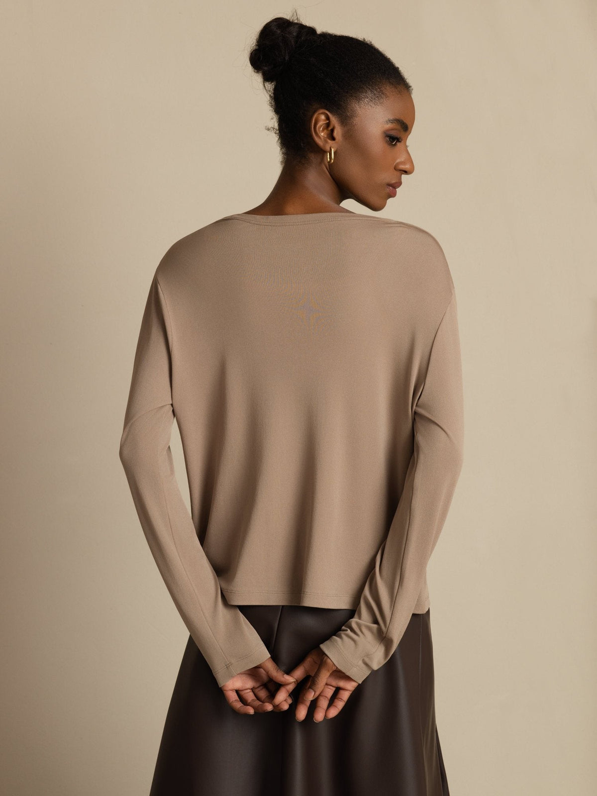 [Tan] Rear upper-body view of a beige cardigan with dark brown skirt, sleeves gathered over clasped hands. 002