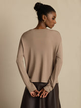[Tan] Rear upper-body view of a beige cardigan with dark brown skirt, sleeves gathered over clasped hands. 002