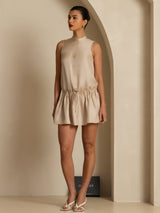 [Tan] Full front view: tan sleeveless drop-waist mini dress with gathered ruffle hem, with the silhouette and hem visible. 006