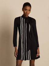 [Black] Black long-sleeve tunic mini dress with vertical white stripes in an angled view, with the model turned. 003