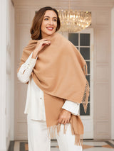 [Tan] tan beige rectangular shawl with fringed edges, styled front view, wrapped around the neck with one hand at the temple. 001