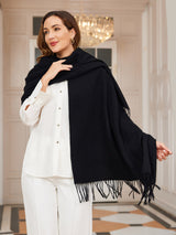 [Black] black rectangular shawl with fringed edges, styled front view, wrapped at the neck with one hand near the chin. 004