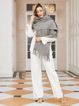 [Gray] medium gray rectangular shawl with fringed edges, styled front view, wrapped at the neck with one hand near the chin. 003