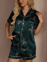 [Emerald Zebra] emerald green animal-print short pajama set with contrast piping, waist-up front view, one hand touching the collar. 005