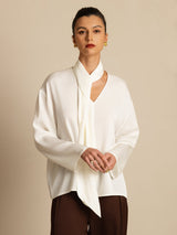[White] Centered upper-body view: white draped-neck long-sleeve blouse with dark brown wide-leg trousers, with arms lowered. 004