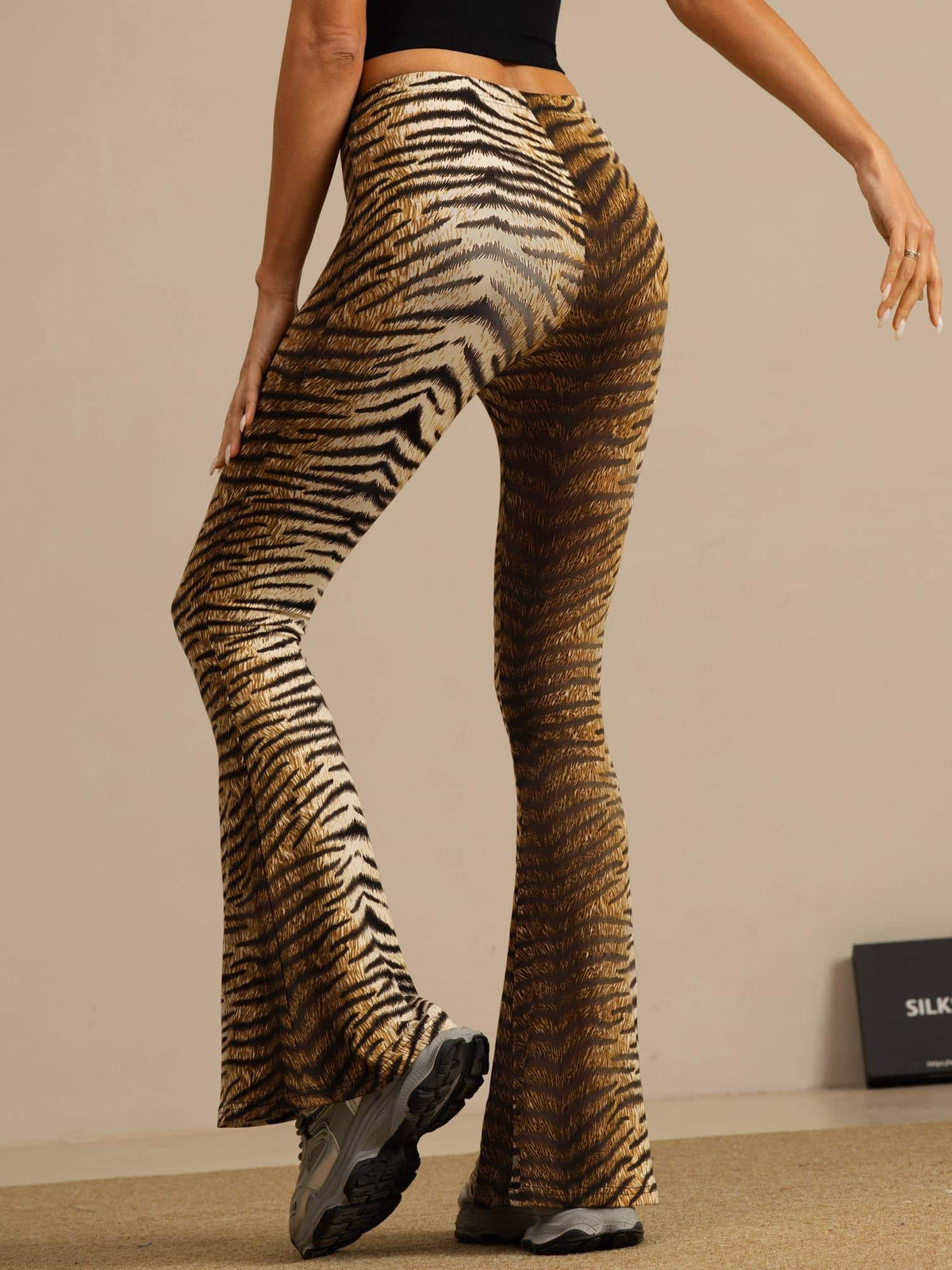 [Tiger] Rear studio view of a model wearing high-waisted flared trousers with a brown-and-black tiger stripe print. 002