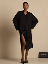 [Black] Front framing captures black draped-neck blouse with a black skirt while one hand rests against the model's waistline. 007